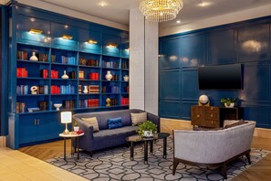 A modern living room with a blue bookshelf, a grey sofa, a coffee table, and a TV mounted on the wall. - Hotel Adagio, Autograph Collection (San Francisco)
