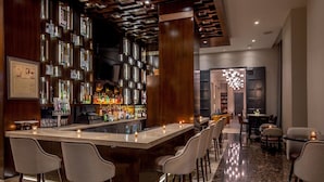 Un espace bar moderne doté d’un long comptoir, de nombreux tabourets et d’une grande variété de bouteilles et de verres.