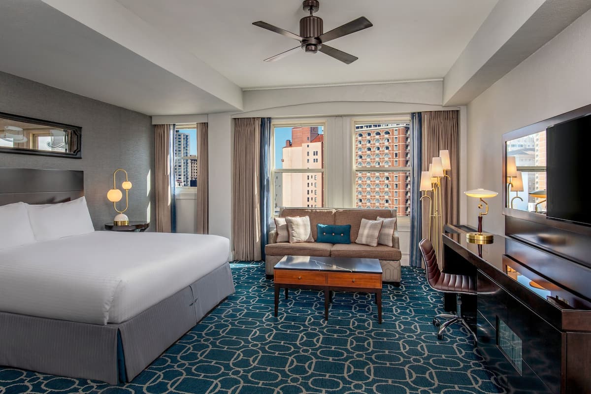 A hotel room with a bed, a sofa, a coffee table, a TV, and a ceiling fan.