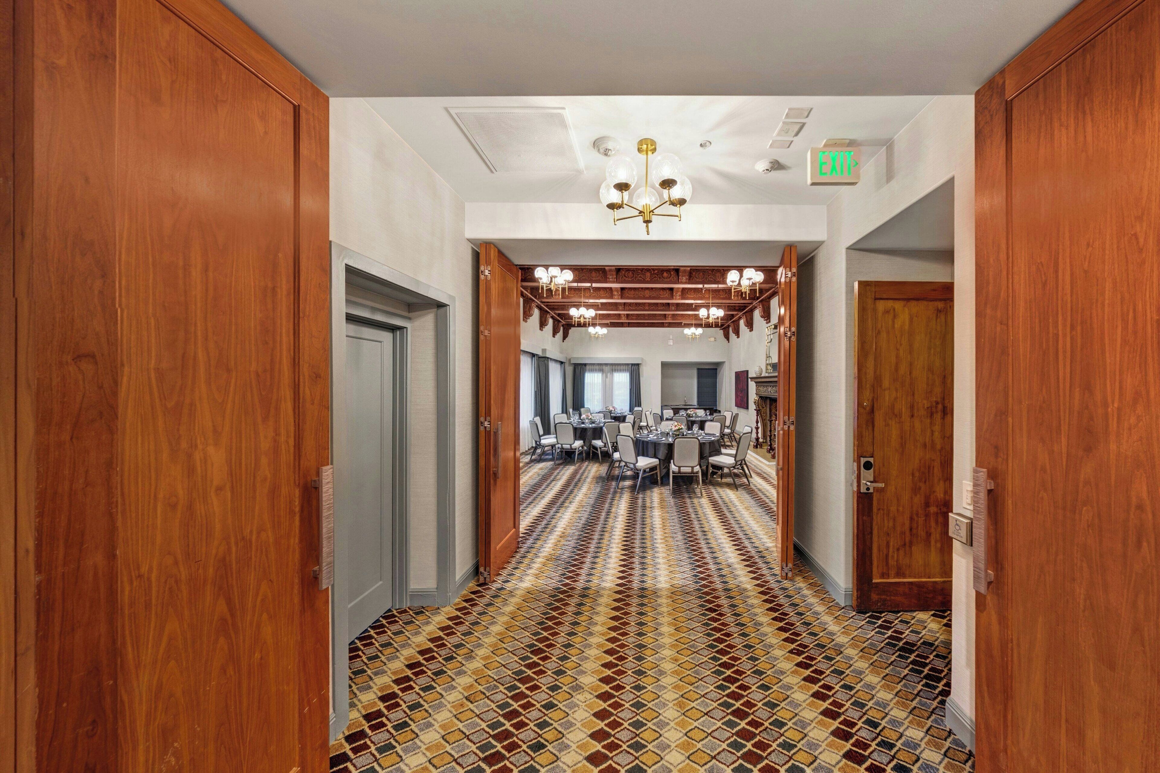 Un couloir d’hôtel avec des portes en bois, une moquette à motifs et un lustre.