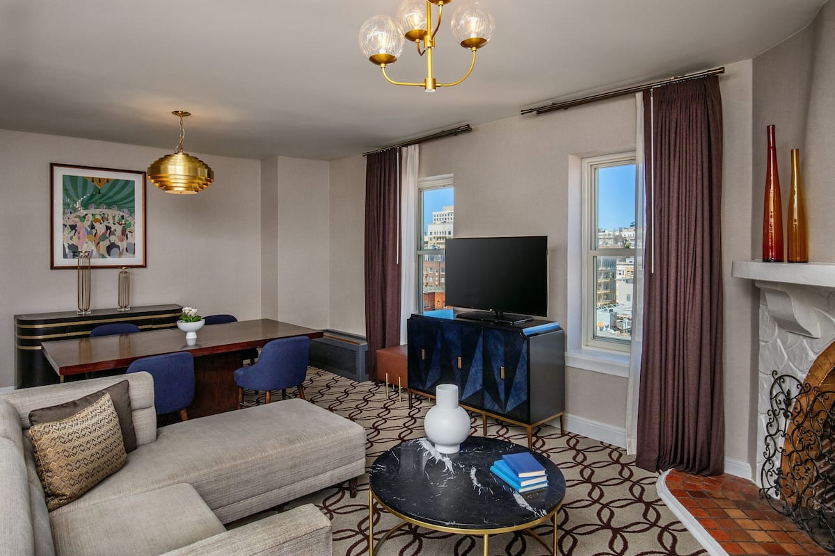 A hotel room with a sofa, a dining table, a TV, and a fireplace.