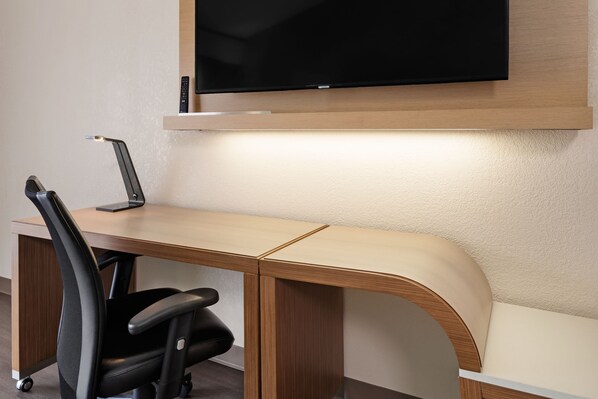 A modern office desk with a flat-screen TV mounted above it, a chair, and a desk lamp.