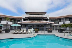 A hotel with a swimming pool, lounge chairs, and umbrellas.