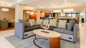 A modern lobby with a sectional sofa, a round coffee table, and a decorative sculpture. - Courtyard by Marriott San Diego Del Mar/Solana Beach (Solana Beach)