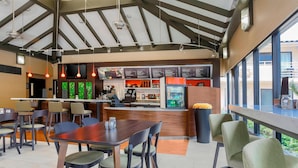 A restaurant with a high ceiling, wooden beams, and a bar area with a menu. Tables and chairs are arranged for dining. - Courtyard by Marriott San Diego Del Mar/Solana Beach (Solana Beach)