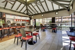 A spacious indoor area with high ceilings, multiple tables and chairs, and large windows offering views of the outside.