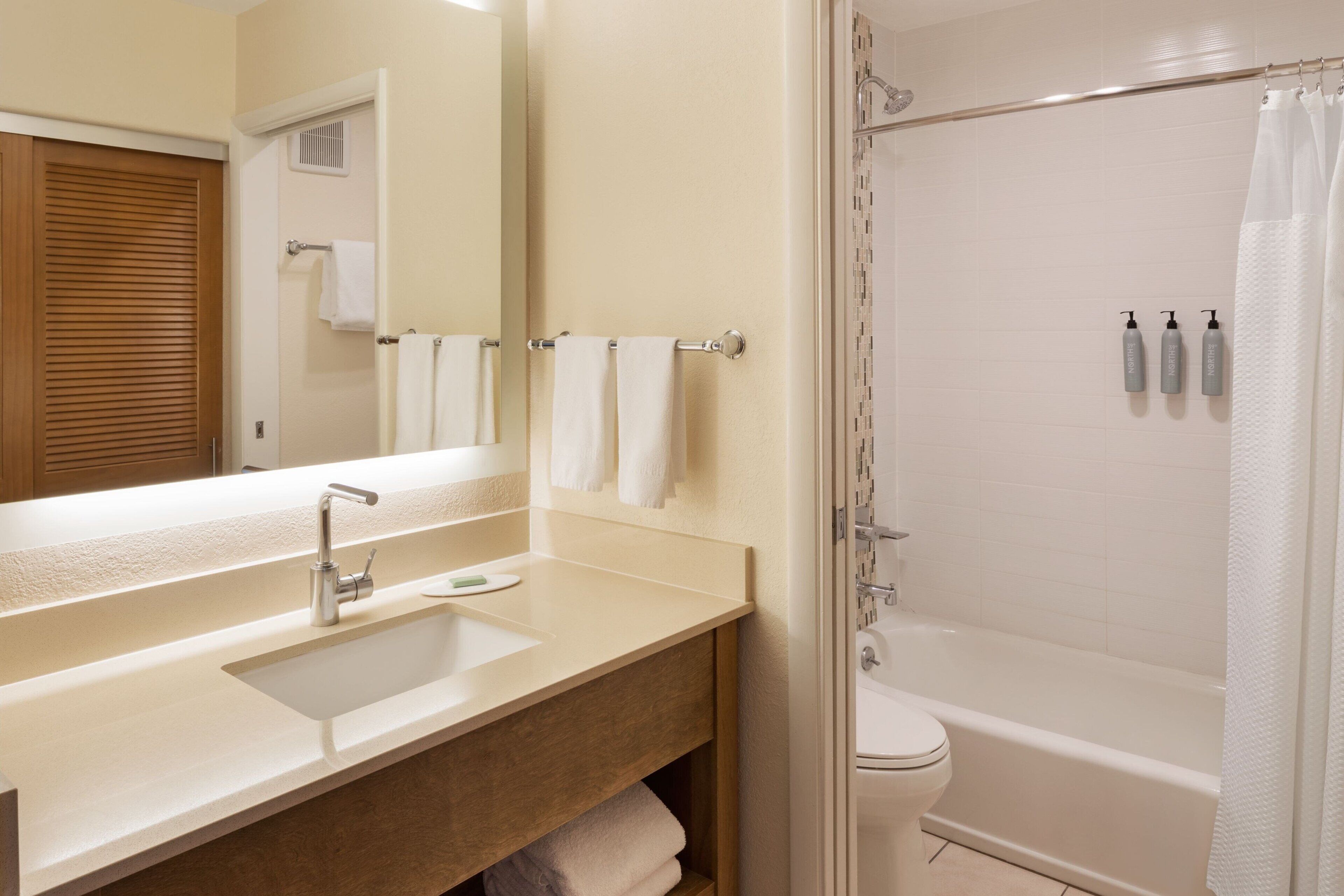 A bathroom with a sink, mirror, towel rack, and a shower area with a curtain.