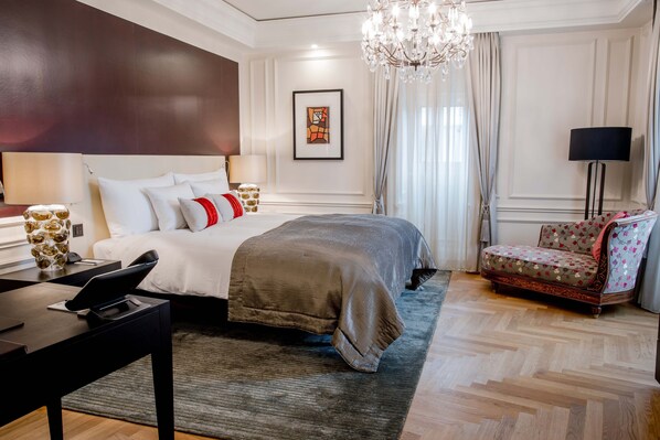A modern hotel room with a large bed, a desk with a laptop, a chair, and a chandelier.