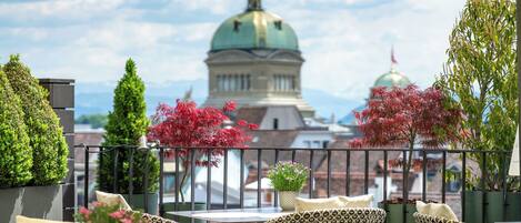 An outdoor seating area with wicker furniture, potted plants, and a view of a building with a dome.
