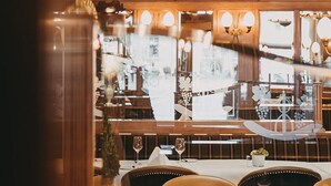 Interior de un restaurante con candelabro, muebles de madera y vistas a la calle a través de amplios ventanales.