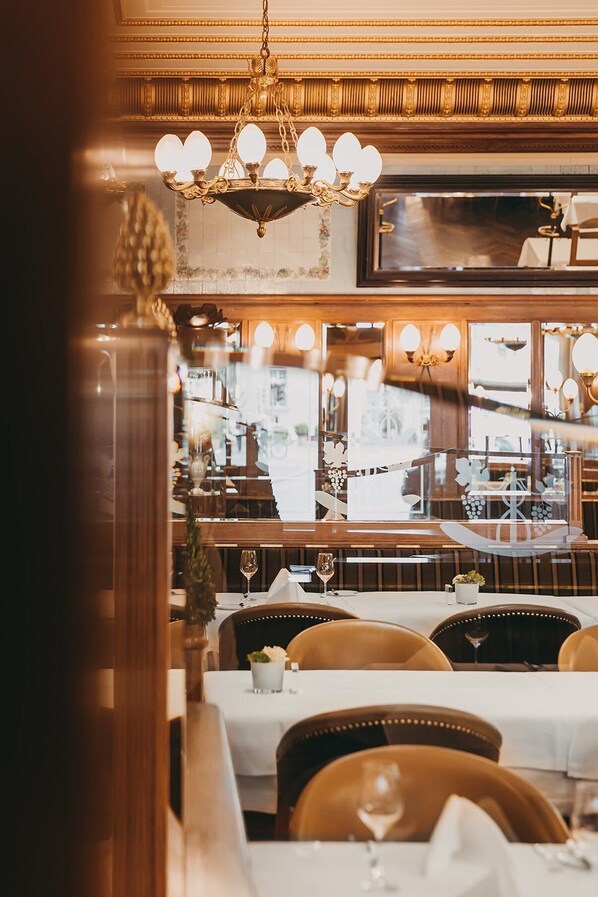 Interior de un restaurante con candelabro, muebles de madera y vistas a la calle a través de amplios ventanales.