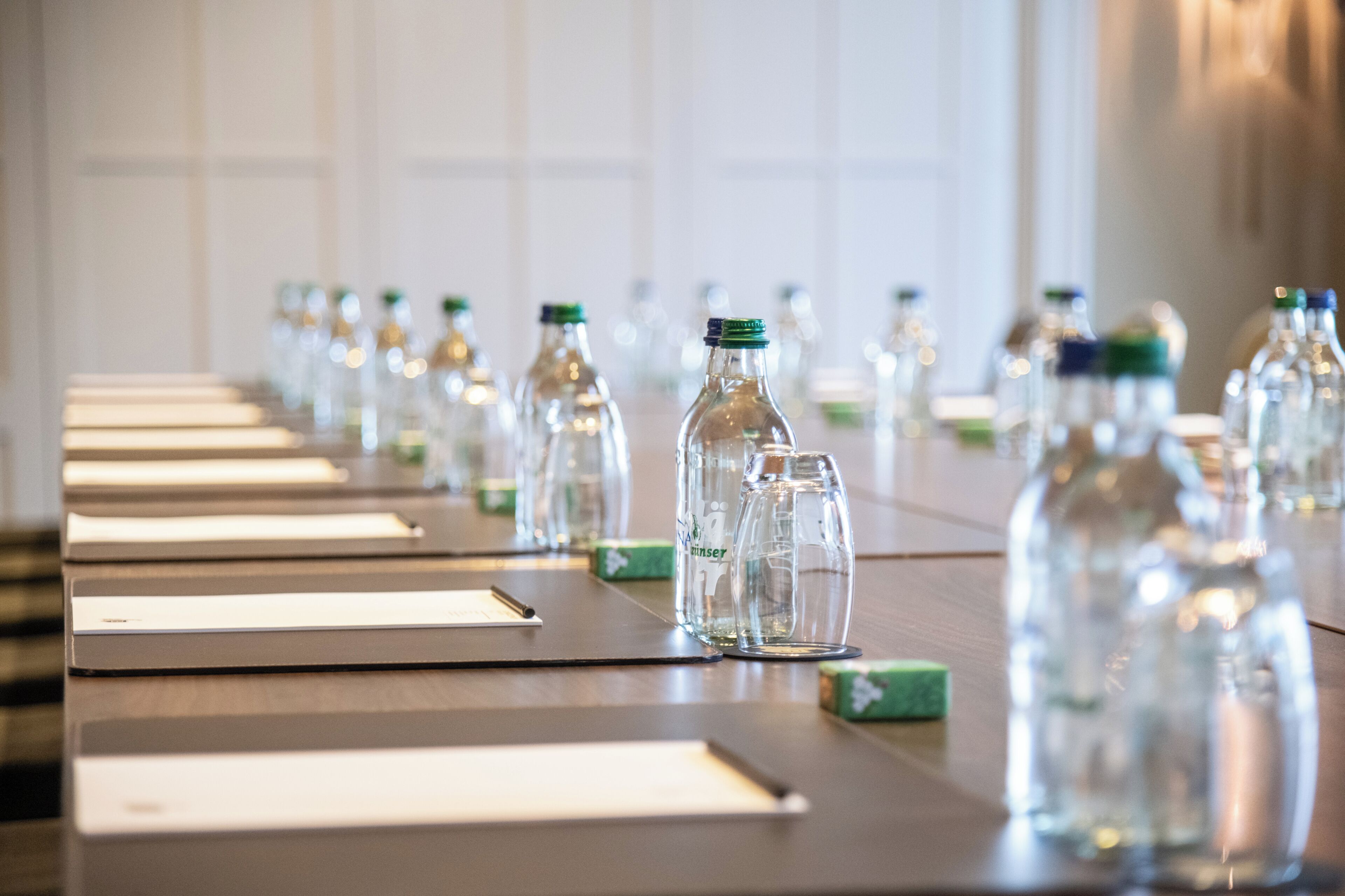 A long table with rows of empty glass bottles and lined papers, likely for a meeting or event.