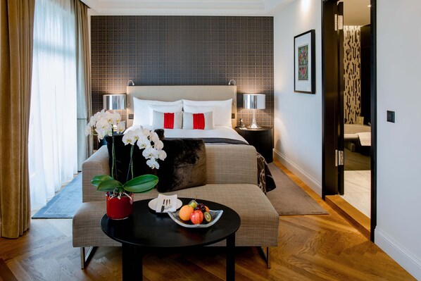 Habitación de hotel moderna con una cama grande, una zona de estar con una mesa y vistas al baño.