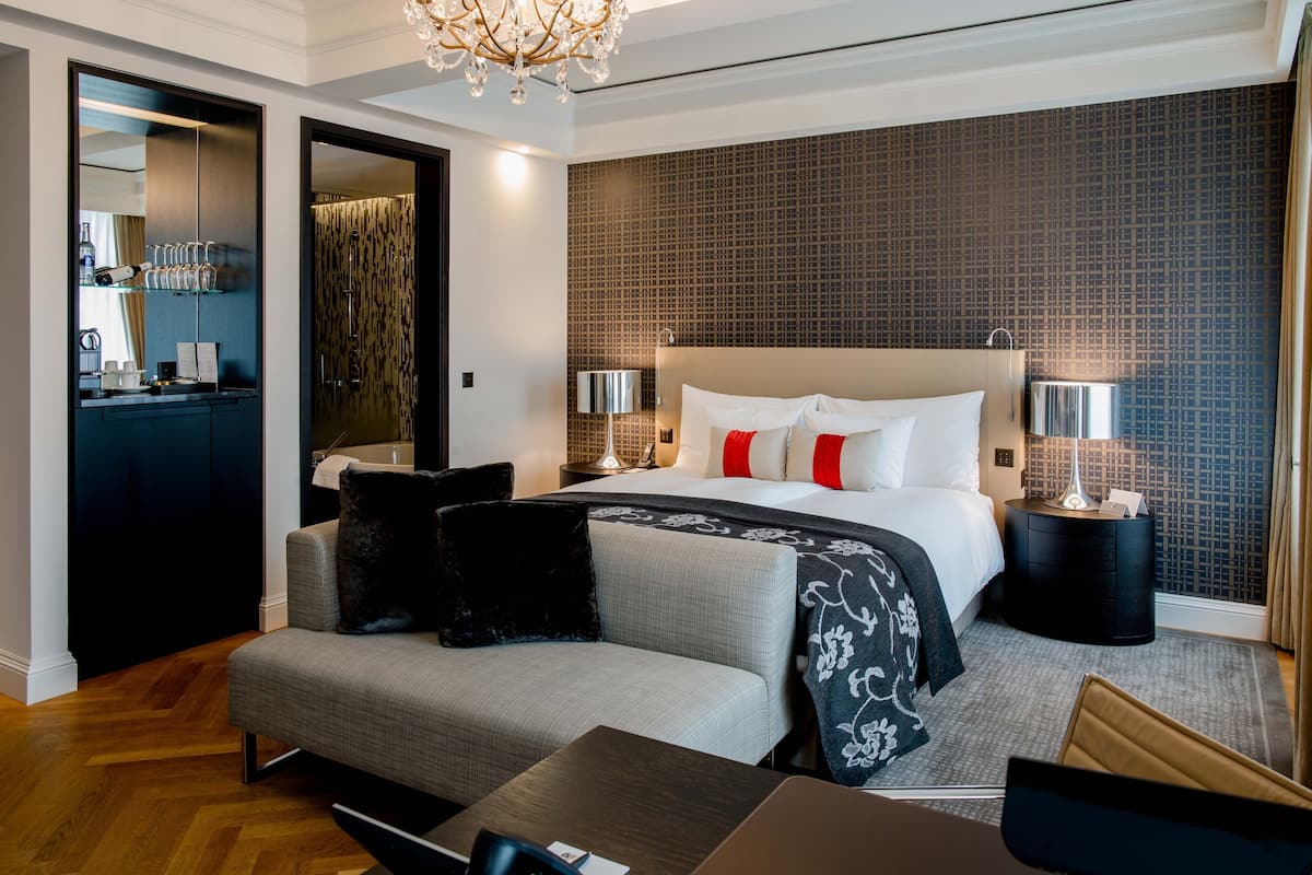 A modern hotel room with a large bed, a sofa, a desk, and a mirror.