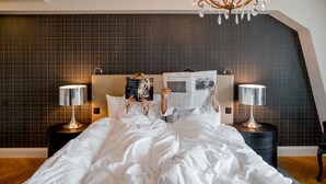 Un dormitorio con una cama grande, dos mesitas de noche con lámparas, un papel tapiz decorativo y una araña.