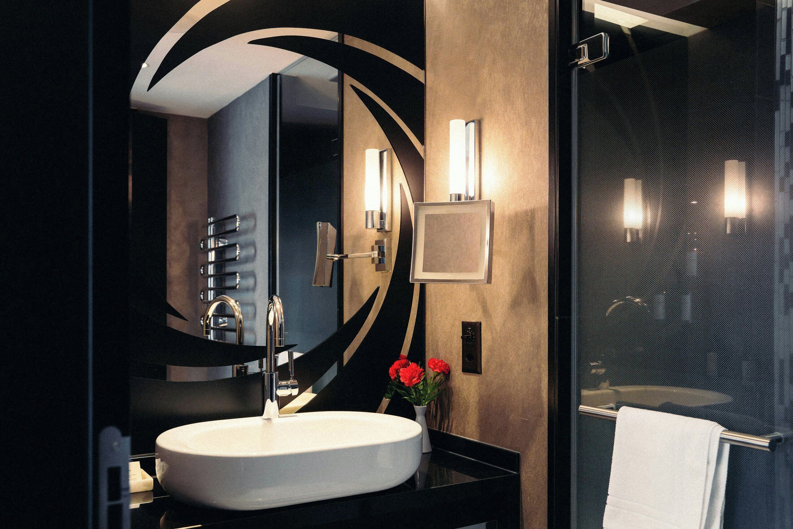 Une salle de bain moderne avec un miroir rond, un lavabo blanc et une cabine de douche en verre.