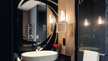 Une salle de bain moderne avec un miroir rond, un lavabo blanc et une cabine de douche en verre.