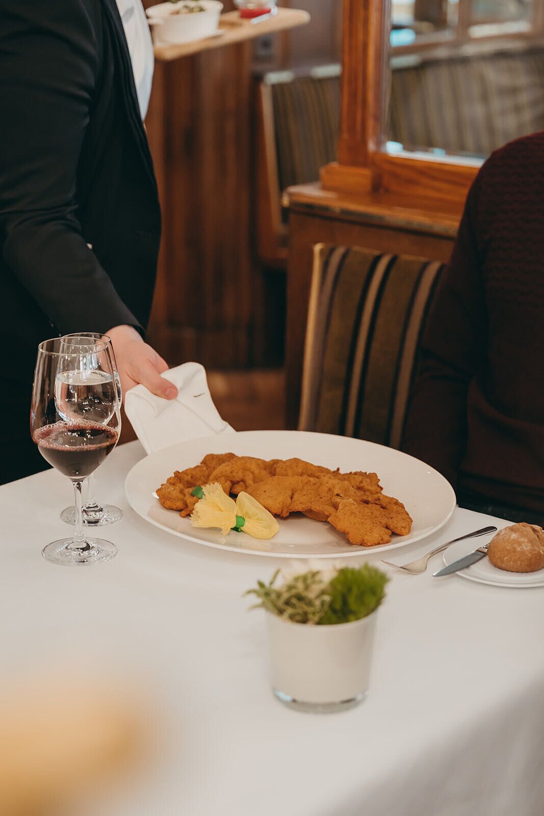 Une table à manger avec une assiette de nourriture frite, un verre de vin rouge et une petite plante en pot.