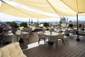 An outdoor terrace with round tables and wicker chairs, overlooking a cityscape with notable buildings and a dome structure.