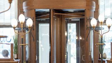 A lobby with a grand wooden door, a large ornate clock, and three wall-mounted light fixtures.
