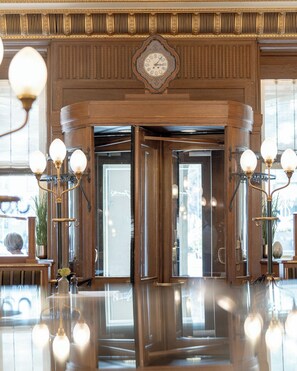 A lobby with a grand wooden door, a large ornate clock, and three wall-mounted light fixtures.