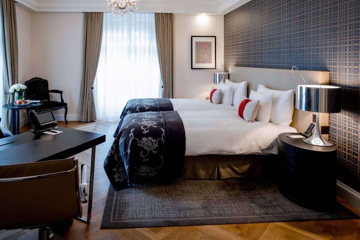 A hotel room with a large bed, a desk with a laptop, a chair, a lamp, and a rug.