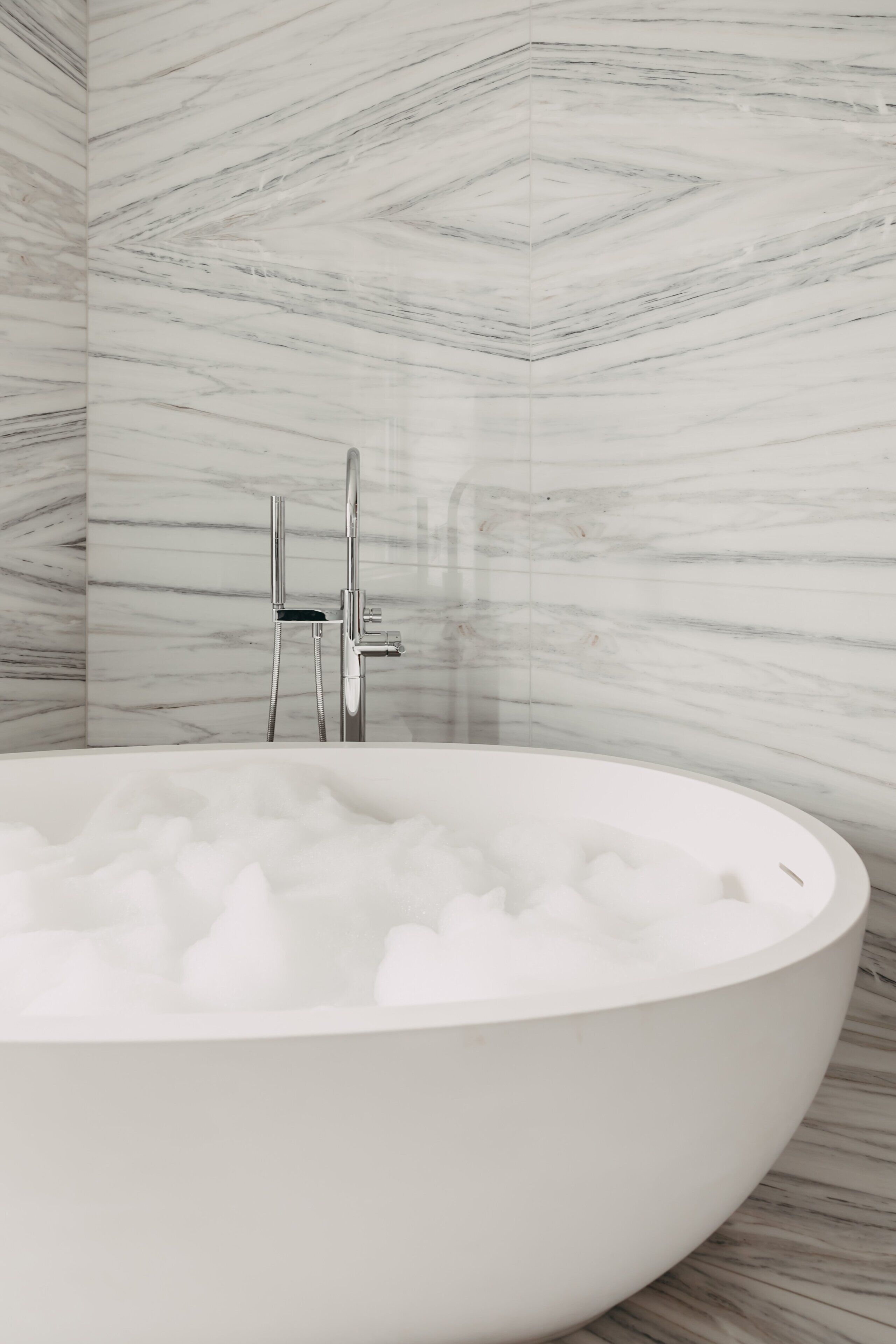 Une salle de bain moderne avec une baignoire îlot remplie de mousse, une douchette à main et un robinet mural.
