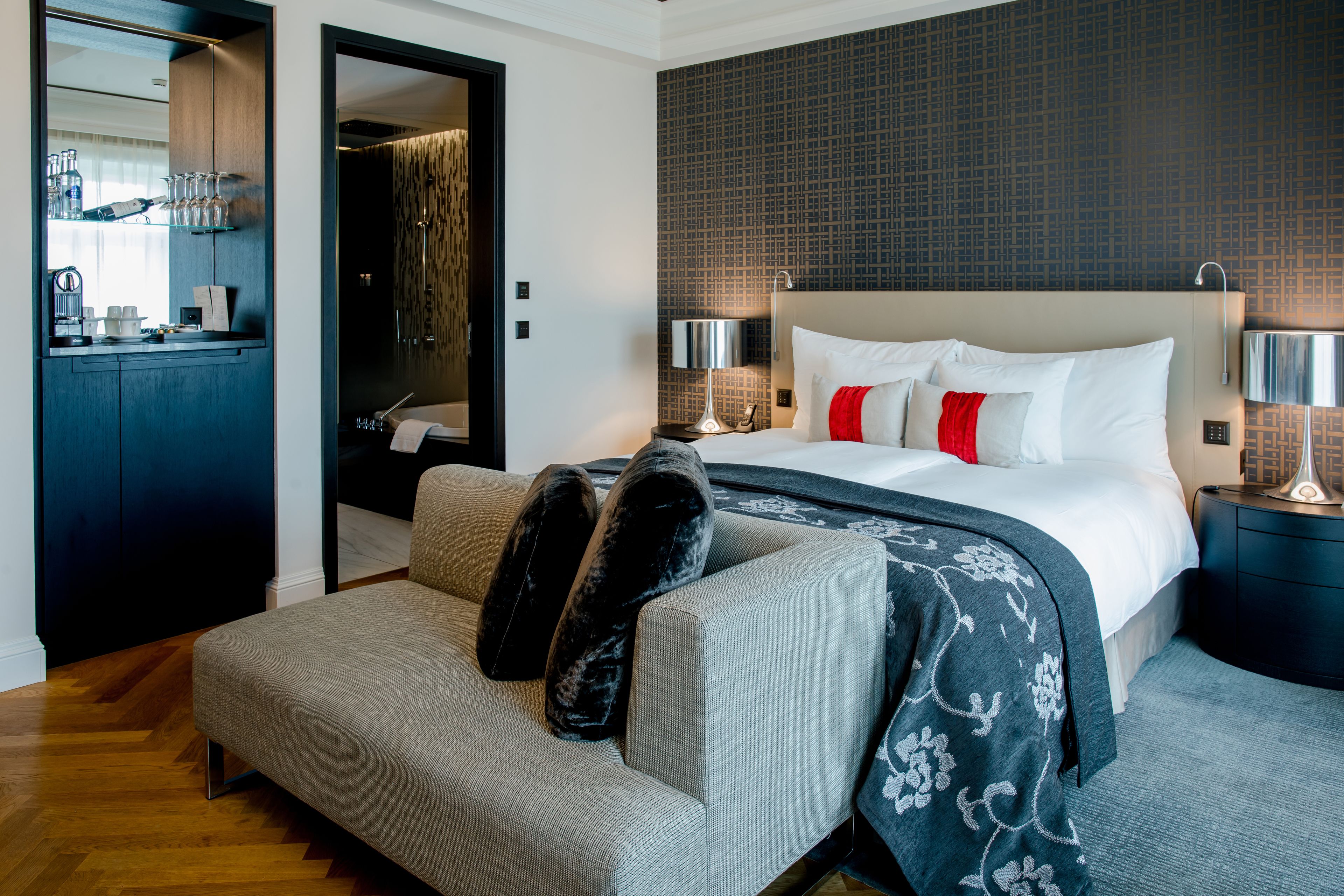 Une chambre d’hôtel moderne équipée d’un lit, d’un canapé, d’un bureau et d’une salle de bain visible à travers une porte ouverte.