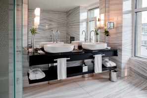 A modern bathroom with two sinks, black vanity, marble walls, and a large window.