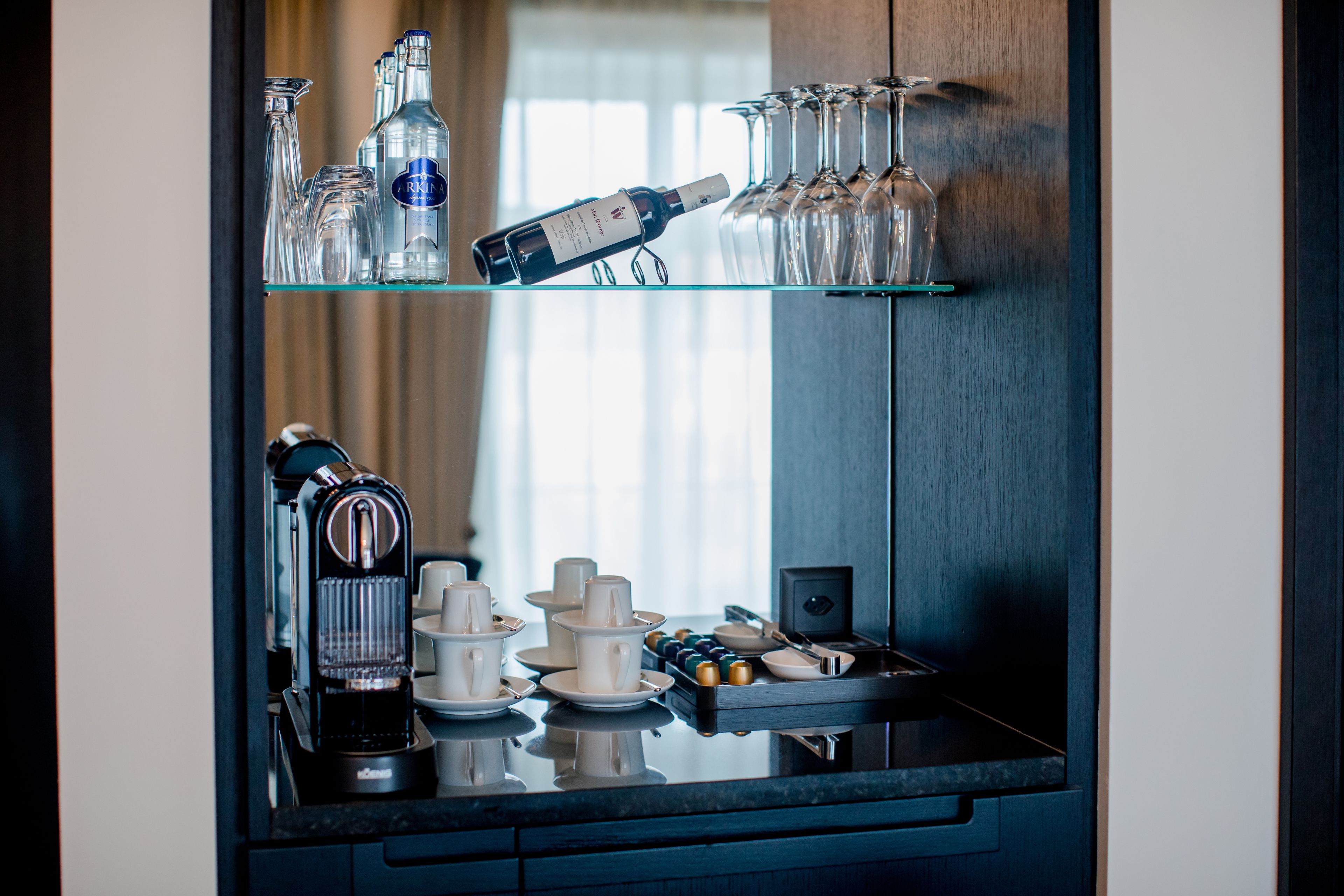Un espace bar avec une machine à café, des bouteilles de vin et des verres disposés sur des étagères.