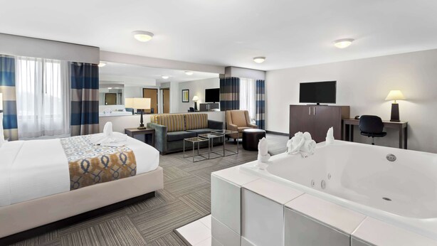 A hotel room with a large bed, a separate sitting area with a sofa and armchair, a television, a desk with a lamp, and a bathtub. - Best Western Naperville Inn (Naperville)