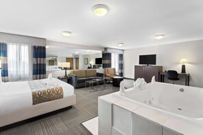 A hotel room with a large bed, a separate sitting area with a sofa and armchair, a television, a desk with a lamp, and a bathtub.