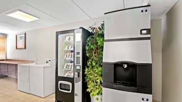 Uma área de lavanderia com máquina de vendas automática, uma planta e um frigorífico.