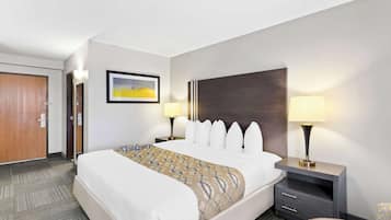 Una habitación de hotel con una cama grande, dos mesitas de noche con lámparas, un cuadro en la pared y una puerta.