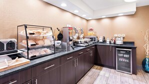 A modern kitchen area with a bread display, coffee machines, and a refrigerator. - Best Western Naperville Inn (Naperville)
