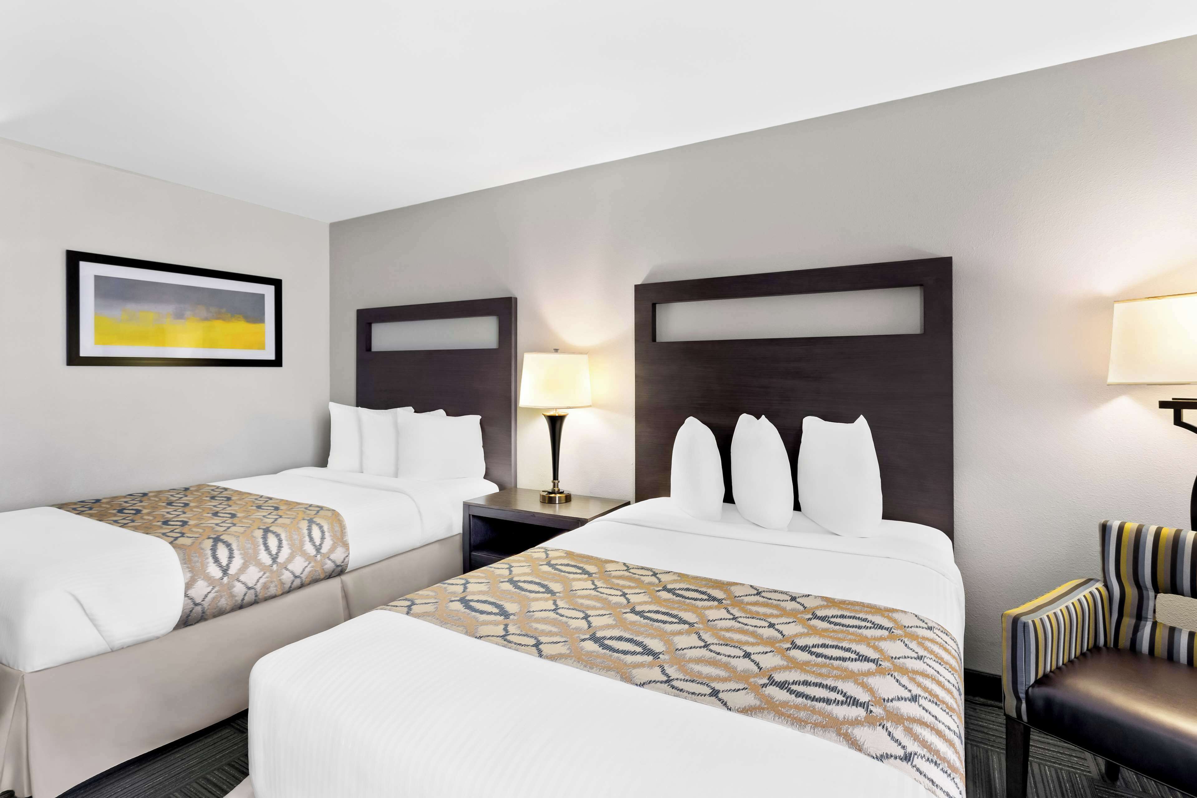 A hotel room with two beds, a nightstand, a chair, and a painting on the wall.