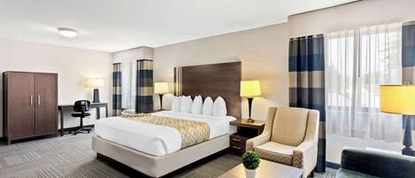 Habitación de hotel con una cama grande, dos mesitas de noche con lámparas, un escritorio con una silla, un sofá y una pequeña mesa con una planta.