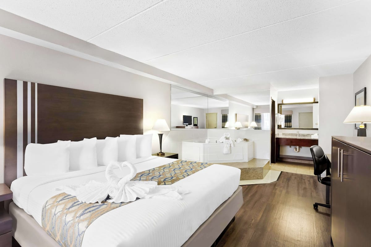 Une chambre d’hôtel comprenant un grand lit, une table de chevet, un bureau, une chaise, un miroir, une coiffeuse et une salle de bain.