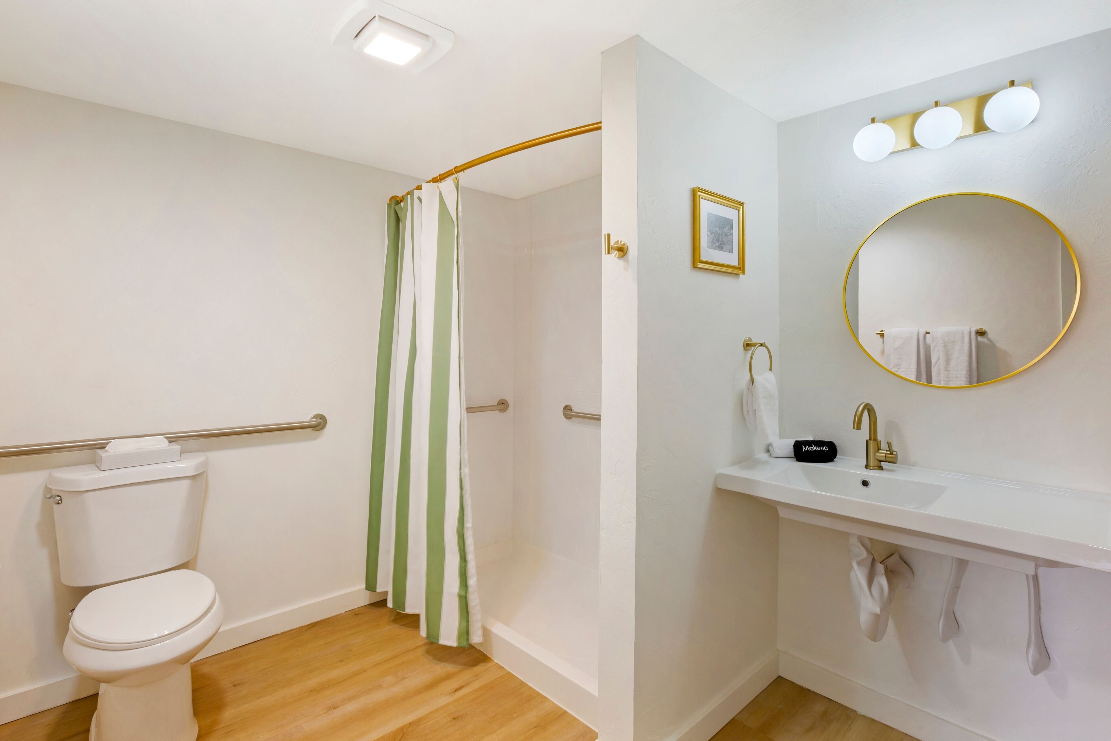 A bathroom with a toilet, a shower with a green and white striped curtain, a sink with a gold faucet, and a mirror with a gold frame.