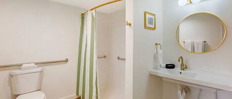 A bathroom with a toilet, a shower with a green and white striped curtain, a sink with a gold faucet, and a mirror with a gold frame.