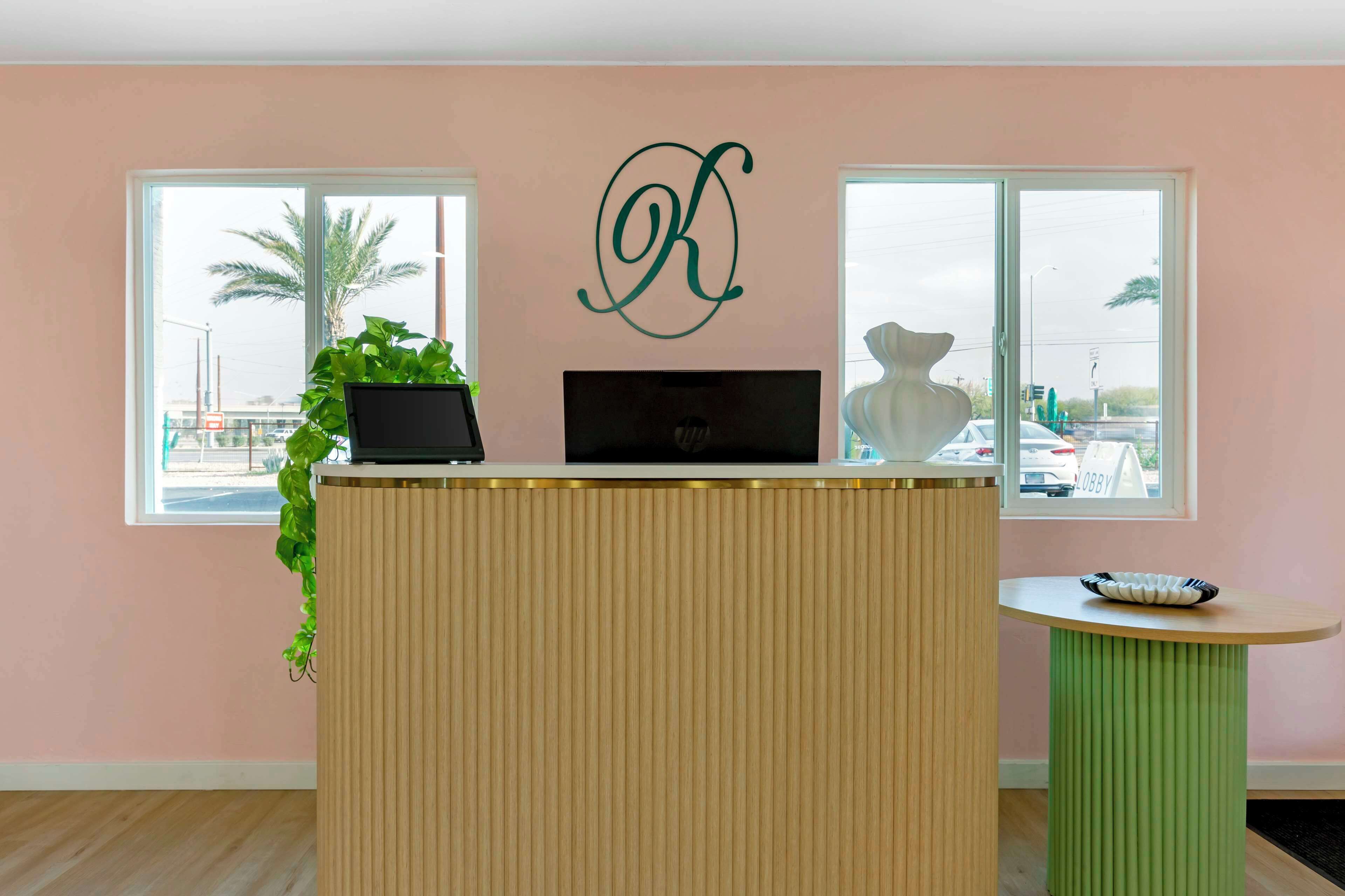 A reception desk with a laptop, a potted plant, and a decorative wall piece.