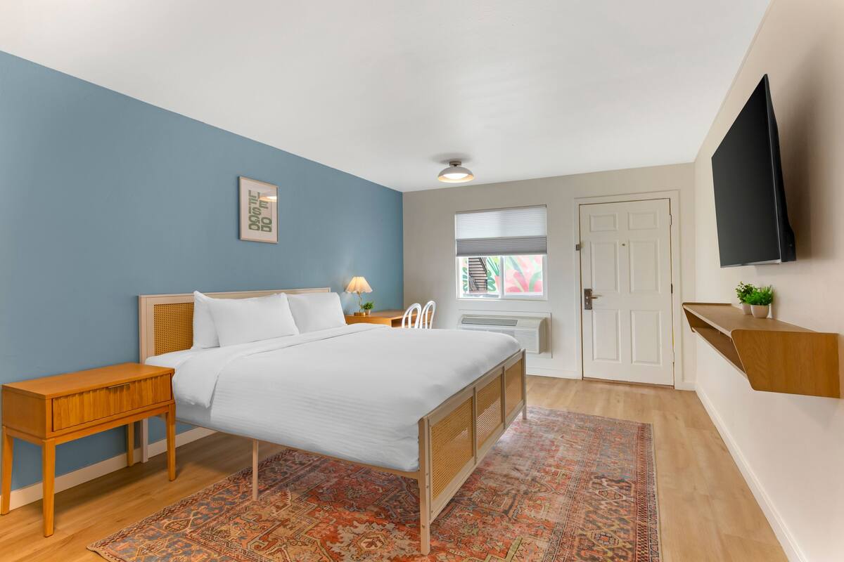 A bedroom with a bed, bedside table, lamp, and a television on the wall.