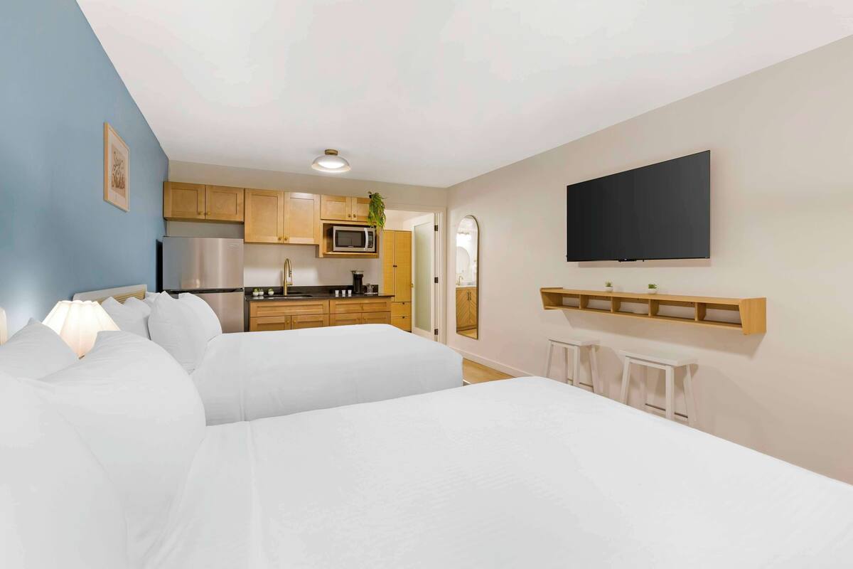 A modern hotel room with a kitchenette, a flat-screen TV, and a large bed.