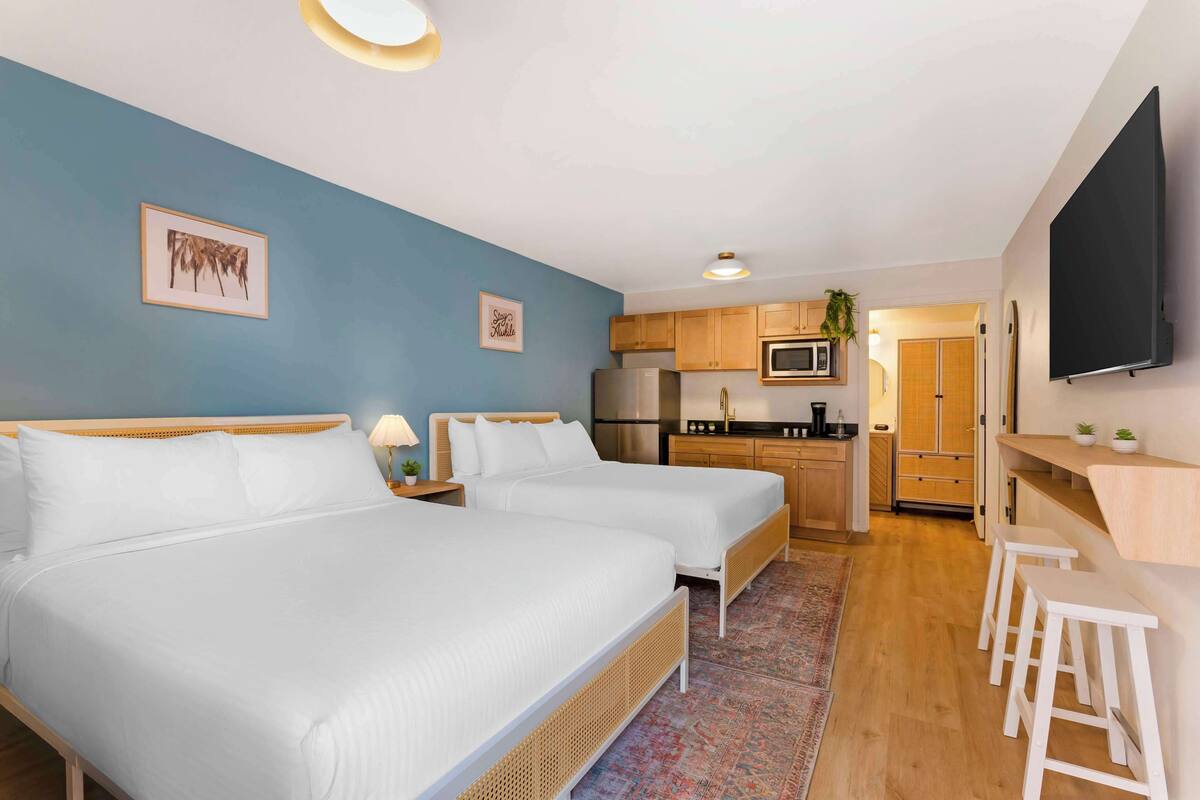 A room with two beds, a kitchenette, a flat-screen TV, and a small bar area.