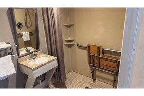 Un baño con lavamanos, espejo, ducha y un banco accesible para sillas de ruedas.
