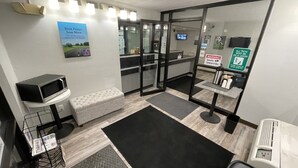 Estación de peluquería para mascotas con piso a cuadros blanco y negro, un banco acolchado blanco, un microondas, una cámara de seguridad y un letrero que indica mantener a las mascotas con correa.