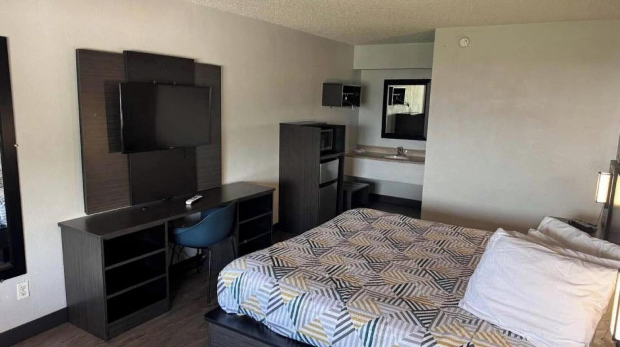 Habitación de hotel con cama, escritorio y silla, televisor, armario y espejo.