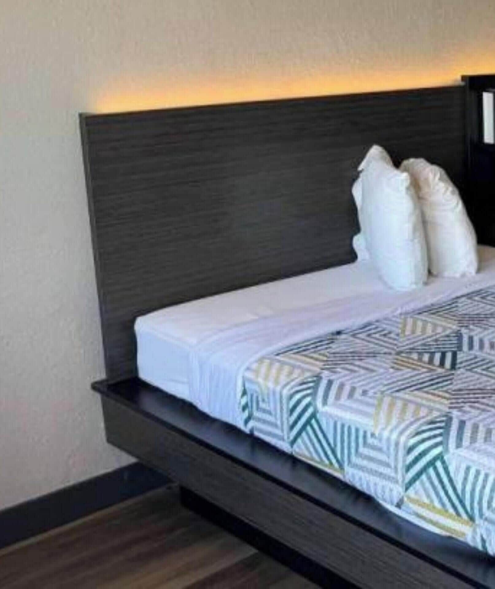 A bed with a dark headboard, white bedding, and a geometric-patterned throw.