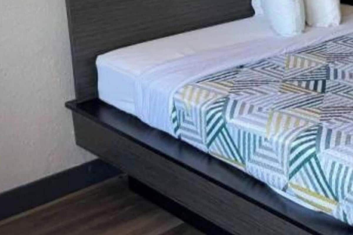 A bed with a dark headboard, white bedding, and a geometric-patterned throw.