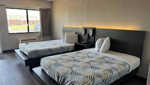 Habitación de hotel con dos camas, una ventana con cortinas, una mesita de noche con lámpara y vistas al exterior.